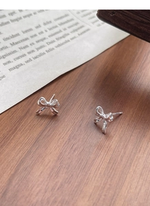 Detailed macro shot of a bow-knot silver stud earring on a rustic wooden background