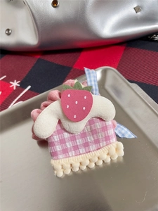 Detailed close-up of pink checkered hair clip with strawberry and plush tassel on tray