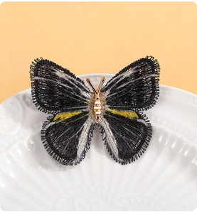 Broche papillon brodée main avec fils noir, jaune et blanc sur un plateau en céramique