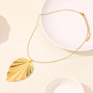 Minimalist stainless steel leaf pendant necklace with golden radial texture on ceramic plate