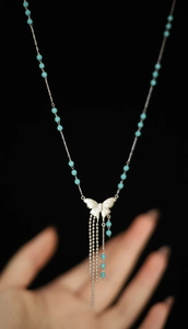 Close-up of silver butterfly pendant with blue beads and long tassels on a steel chain