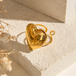 Gros plan d'une bague médaillon coeur dorée polie sur un socle avec fleurs séchées
