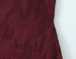 Nahaufnahme von weinrotem Jacquard-Stoff mit strukturierten Rosenmustern und Samt-Finish