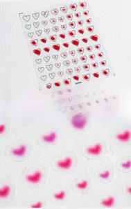 Macro detail of 5D heart nail art stickers featuring red and pink gradient designs