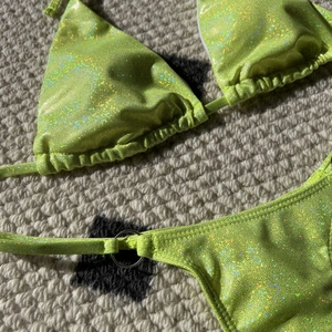 Macro detail of sparkly neon green bikini fabric with metallic silver ring accent
