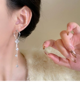 Close-up of silver tassel earrings with zircon stars worn by a model on a beige background