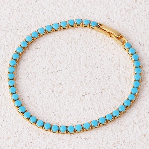 Detailed close-up of a gold tennis bracelet with vibrant green stones on a stone surface