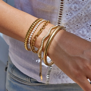 Détail de bracelets et jonc superposés en acier inoxydable plaqué or 18 carats au poignet