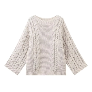 Detailed close-up of textured cable knit pattern and wavy hem on a beige sweater