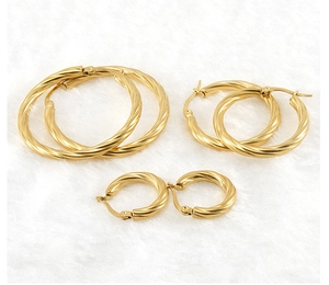 Detailed view of three sizes of gold-plated twisted hoop earrings on soft white texture