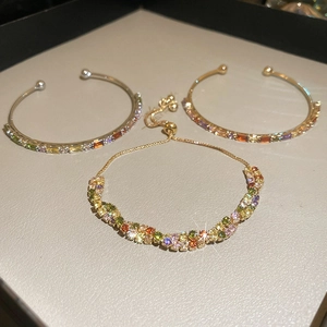 Macro shot of gold-plated bracelets with colorful zircon stones on grey velvet display