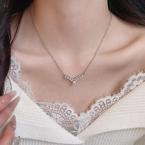 Close-up of a silver V-shaped pearl pendant necklace on a woman's neck and collarbone
