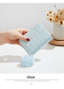 Detail of light blue faux leather purse with white daisy embroidery and a fur pompom
