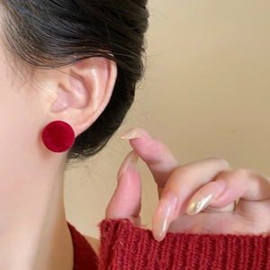 Close-up of red flocked round stud earring on model showing soft velvet texture