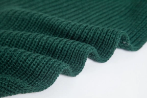 Close-up of dark green knitted acrylic texture and fabric pattern of the sleeved scarf