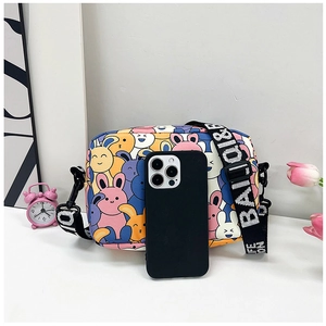 Detail of cartoon rabbit crossbody bag with wide letter strap beside a phone and clock