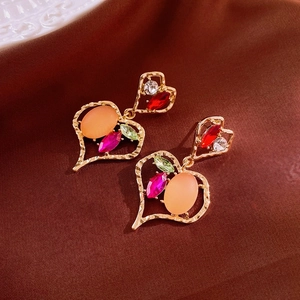 Détail macro de boucles d'oreilles cœur dorées avec cristaux colorés sur soie brune