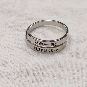 Macro shot of silver wrap ring with BE FEARLESS engraving on textured linen background