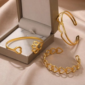 Detailed close-up of three gold hollow heart and paw print cuff bracelets on satin fabric