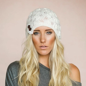 Close-up of white knitted beanie featuring intricate leaf lace pattern and decorative buttons.