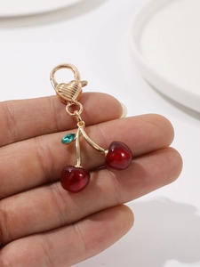 Close-up of red cherry pendant with golden heart lobster clasp and green leaf detail