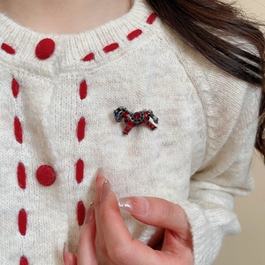 Détail d'une broche cheval en émail avec pierre rouge sur un cardigan tricoté