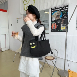 Close-up of black canvas tote bag featuring yellow cartoon cat embroidery and ear detail