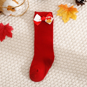 Close-up of red Christmas baby socks with knit bows and small golden bells on a soft rug