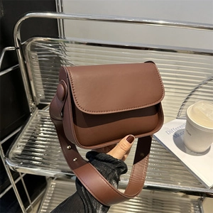 Detail of a brown PU leather crescent shoulder bag with wide strap in a lifestyle setting