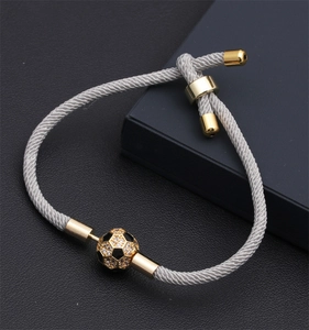 Dettaglio del bracciale da calcio grigio intrecciato con ciondolo dorato e cristalli