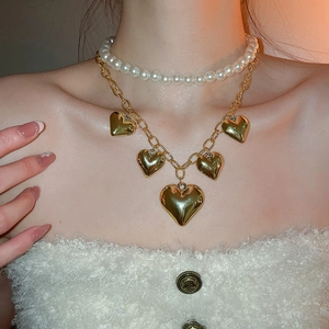 Close-up of double-layered necklace featuring white pearls and golden heart charms