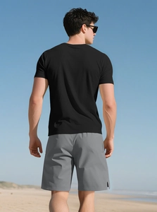 Outdoor back view of men's slim fit black t-shirt and grey shorts on a sunny beach