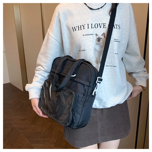 Detailed view of black canvas crossbody bag with mesh pocket and white buckles