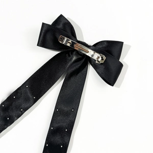Elegant black bow hair clip with pearl ribbons and metal spring clip on white background