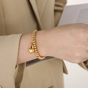 Detail of 18K gold-plated beaded heart bracelet worn on wrist over beige suit blazer