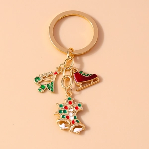 Golden Christmas keychain with enamel tree, sled, and bell charms on beige background