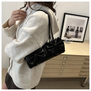 Detail of a black cylindrical Boston bag with two large decorative bows and dual handles