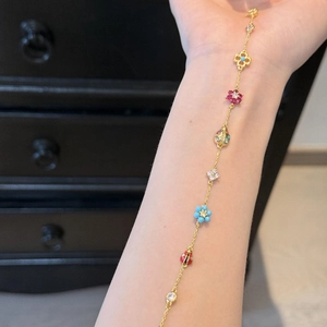 Golden bracelet with colorful enamel ladybug and flower pendants on a model's wrist