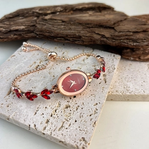Detail view of oval rose gold watch with red dial and leaf-shaped gemstones on stone