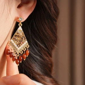 Primer plano de pendientes vintage en forma de rombo dorado con diamantes y borlas de cuentas.