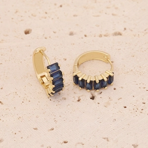 Detail of gold hoops with emerald-cut dark blue zircon stones on textured stone