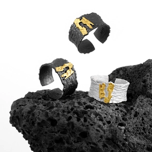Artistic S925 silver textured rings in black and gold finish on volcanic rock base