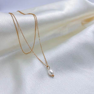 Detailed view of elegant white pearl pendant on a gold necklace over white satin fabric