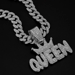 Macro detail of silver Cuban link chain with iced-out QUEEN crown pendant on black background