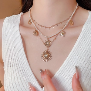 Detail of layered gold sun pendant necklace with small white pearls on a female model
