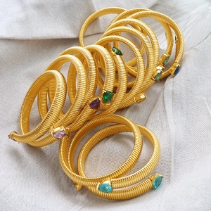 Golden snake-shaped elastic bracelet with colorful pear-cut gemstone accents on fabric