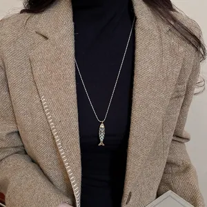 Blue enamel fish pendant necklace with golden chain on a black turtleneck sweater
