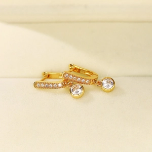 Detail of gold-plated hoop earrings featuring micro-pave zircons and a round solitaire drop