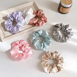 Close-up of assorted satin silk scrunchies in pastel colors on a minimalist display tray