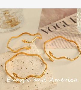 Detail of three gold snake-shaped bangles with wave curves on a textured stone base